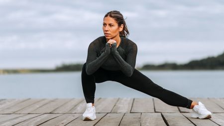 Woman performing a Cossack squat with right knee bent and left knee extended with backdrop of a river 