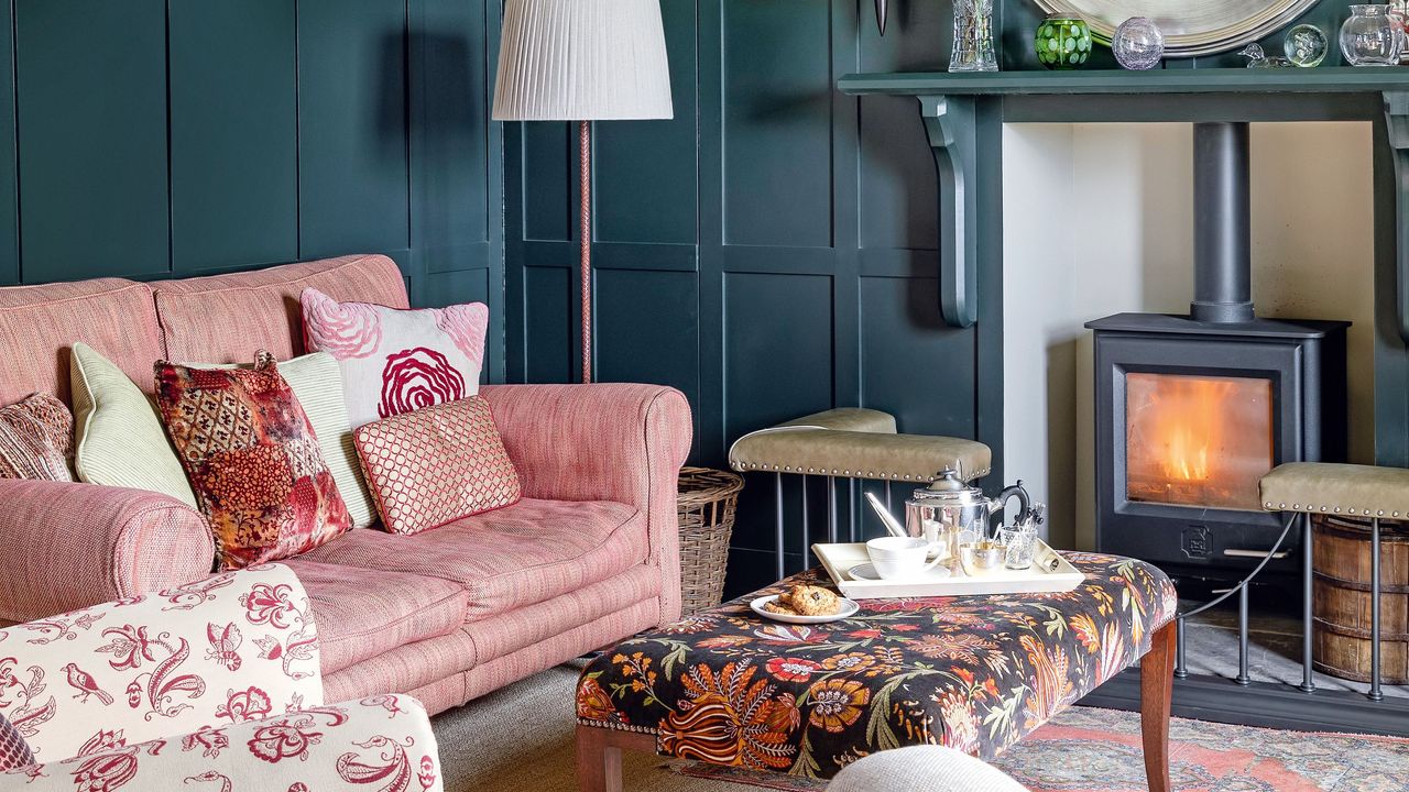 Snug room ideas with dark panelled walls, pink sofa and light ceiling with lamps and wood-burner