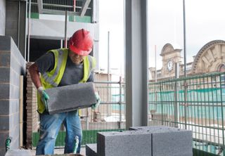 Building materials on a construction site with a builder in a high-vis jacket moving building blocks