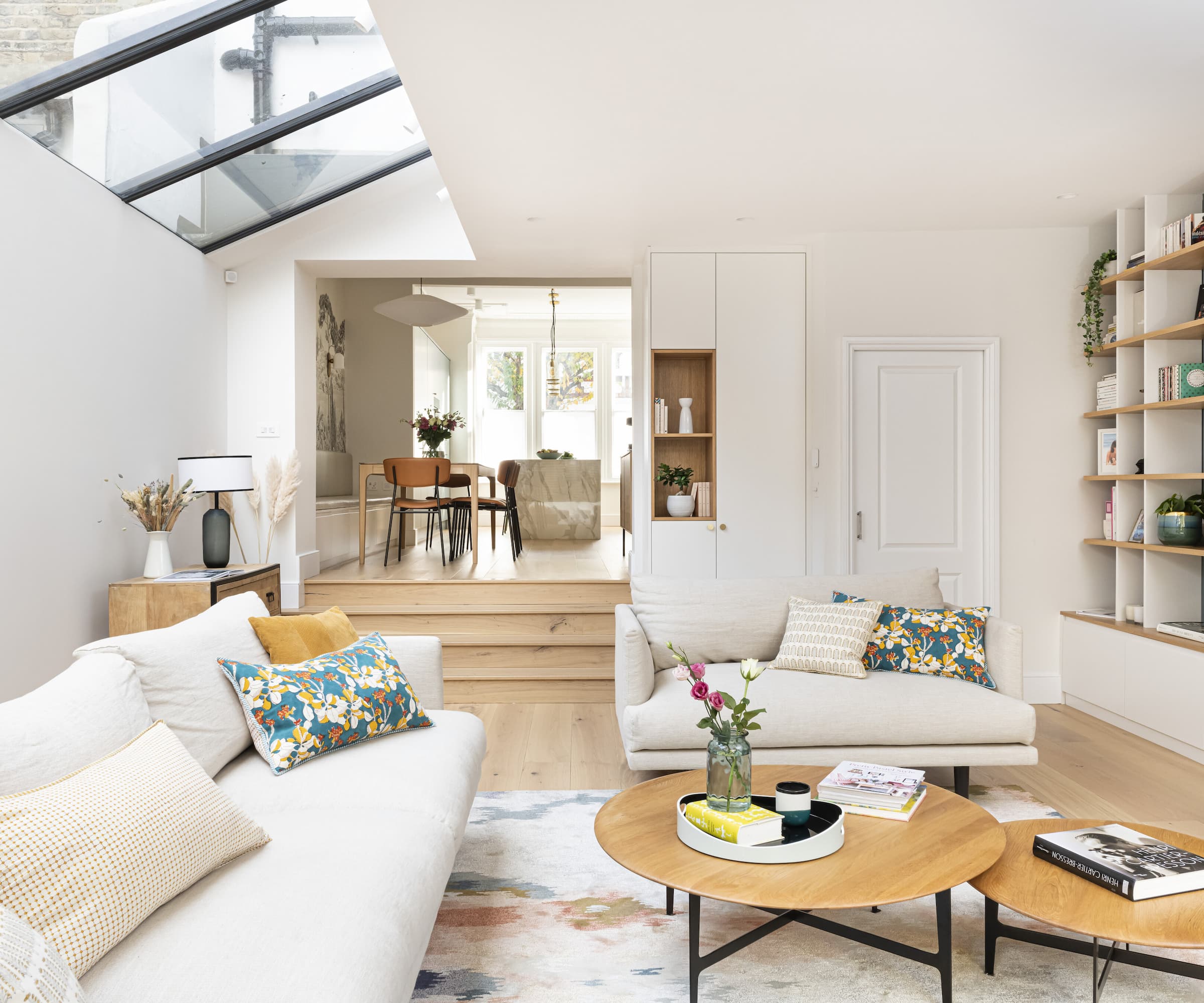 A living room with rooflights above and wooden flooring and white walls and ceilings