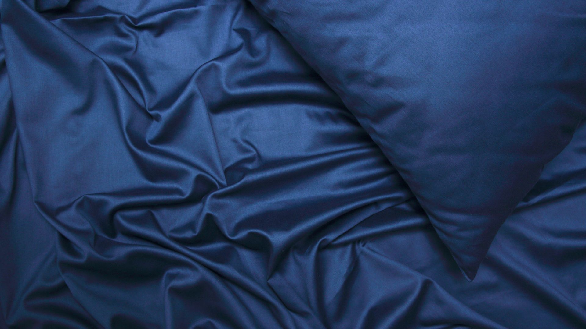A close-up shot of dark blue satin bedding, including a pillow and sheets.