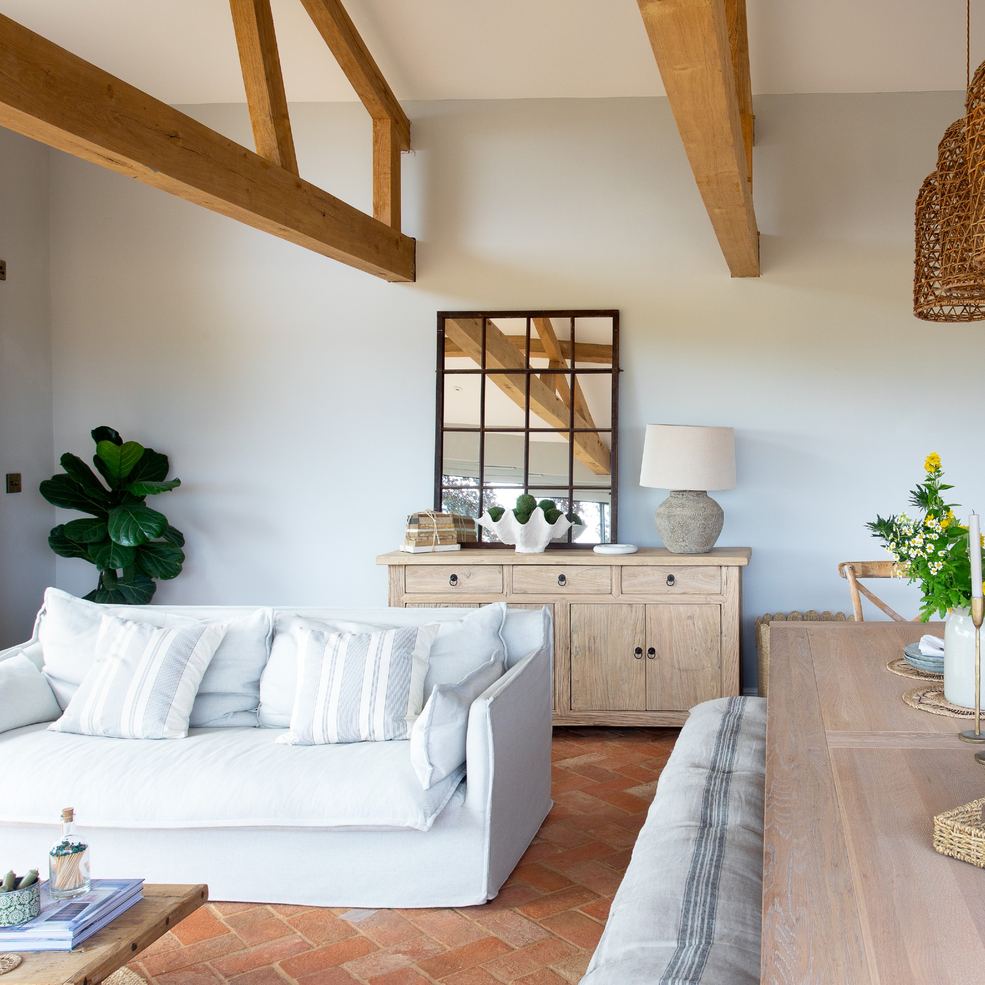 An open-plan living room with a white sofa, terracotta tiled floor and wood furniture