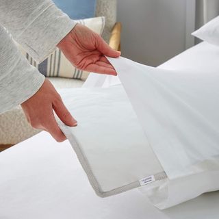 A pair of hands placing the Silentnight Cooling Gel Pillow Pad inside a white pillowcase