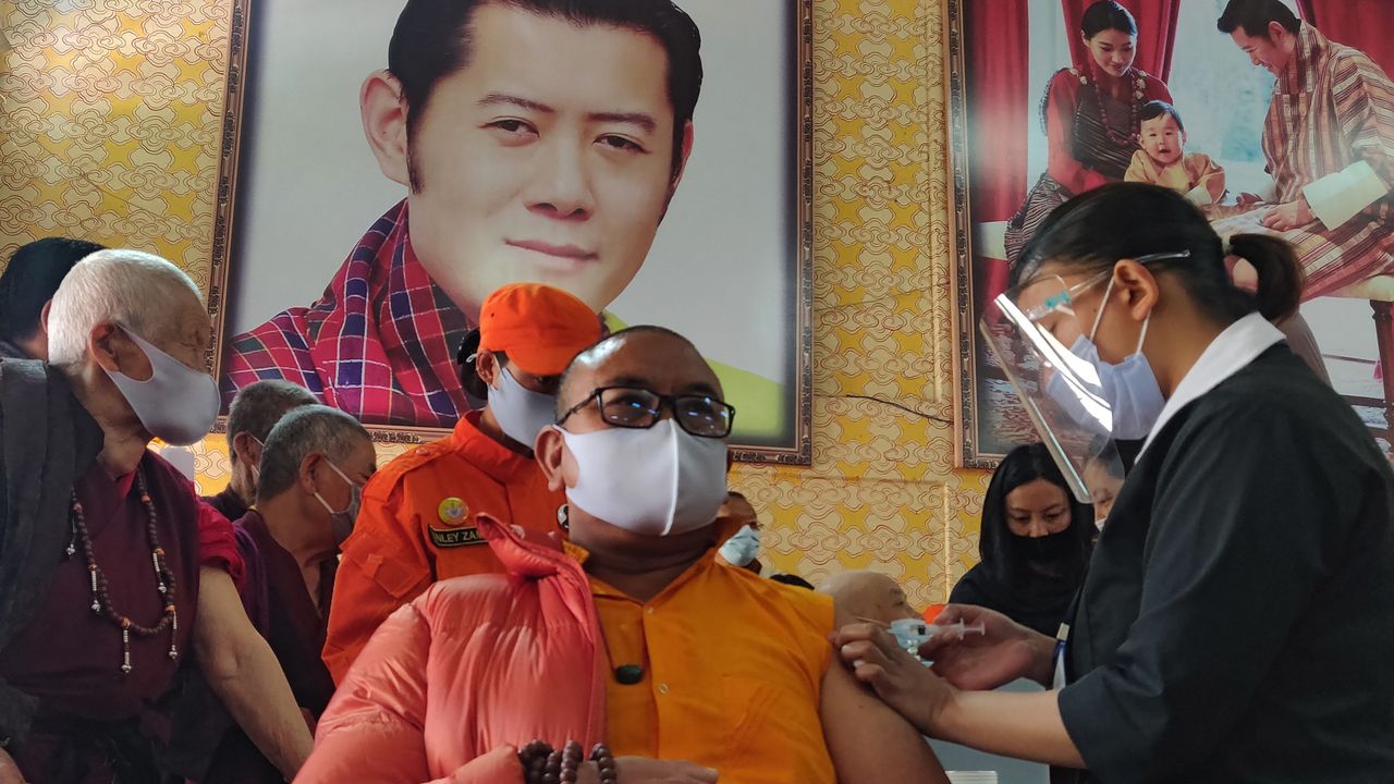 A Buddhist monk receives a vaccine below an image of King Jigme Khesar Namgyel Wangchuck