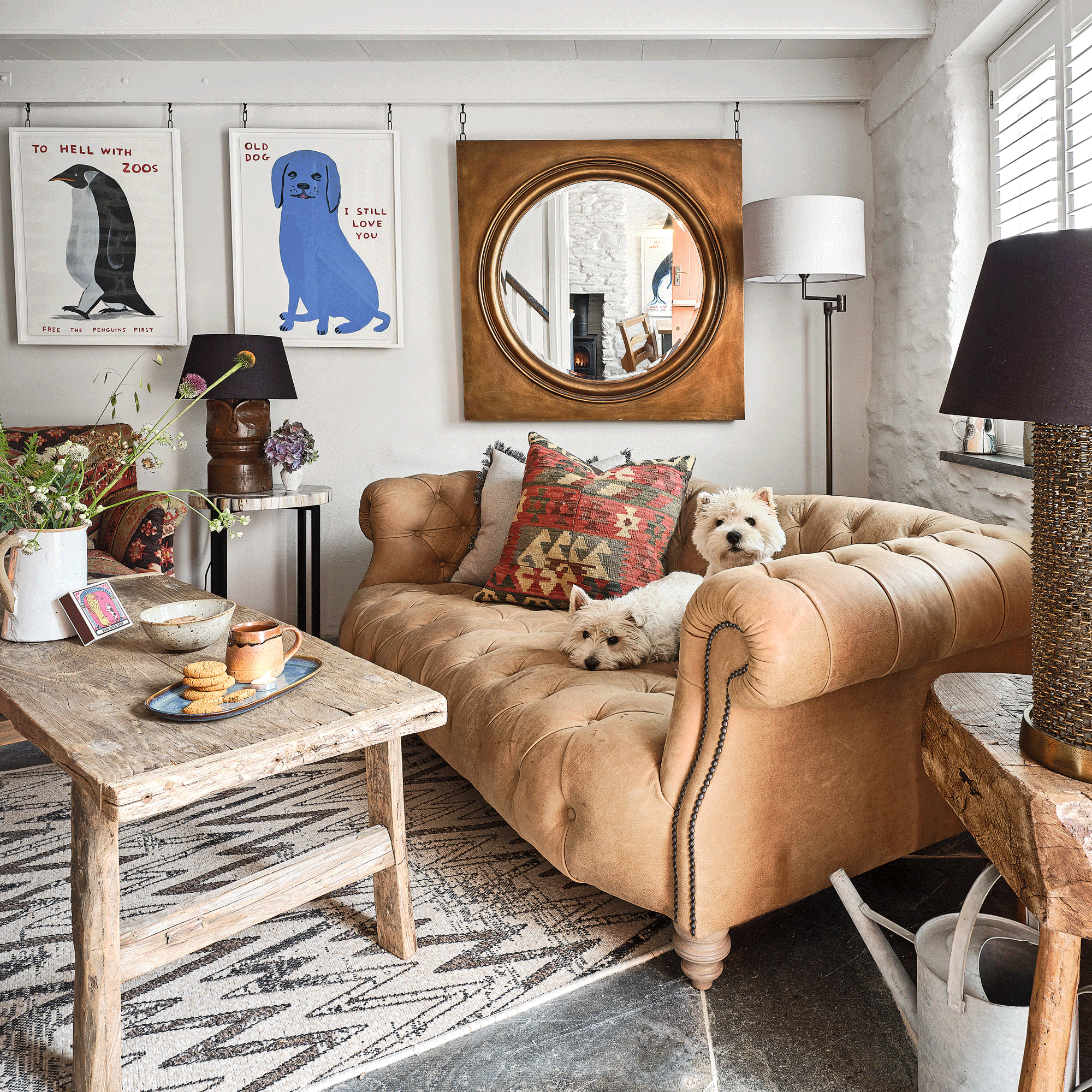 a living room with a large leather chesterfield style sofa, a rustic coffee table patterned rug and cushion and a statement gold framed mirror