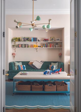 A living room with an alcove bookshelf, a green sofa, a blue rug and a coffee table with wicker storage baskets underneath