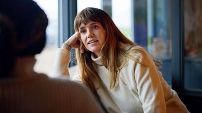 Woman leaning on one arm sitting on sofa talking to friend