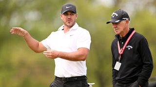 Brooks Koepka of the United States talks with Coach Pete Cowen as they walk off the ninth tee during a practice round prior to the 2023 PGA Championship at Oak Hill