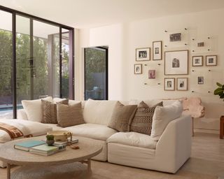 Large, bright living room, minimalist style with cream sofa, photo gallery wall, round coffee table
