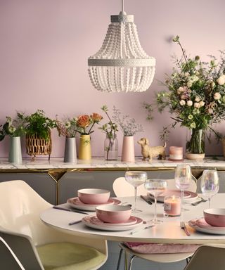 Pink floral dining area with bead chandelier and and shelving with vases of flowers
