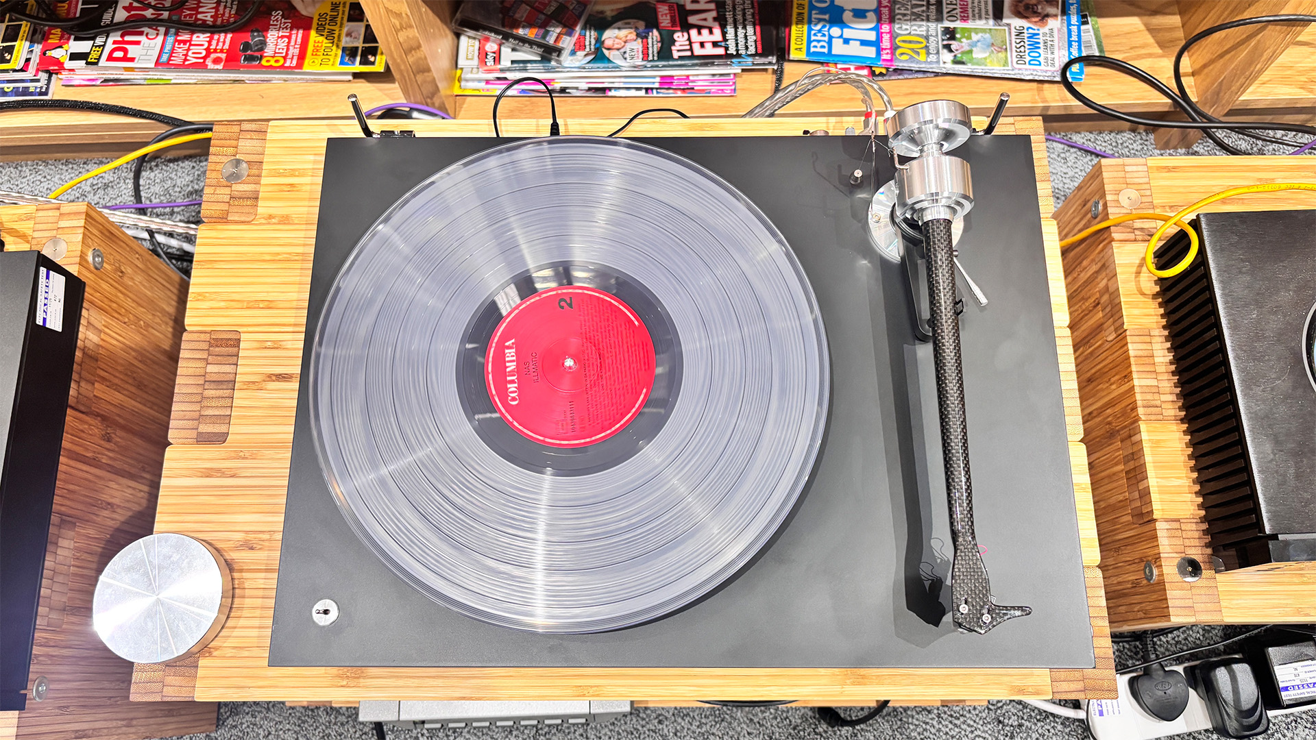 Pro-Ject Debut Reference 10 turntable on wooden hi-fi rack in front of bookcase with clear vinyl record on platter, viewed from above
