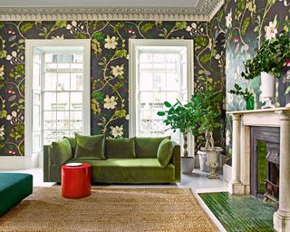 Large living room with dark floral wallpaper, bright green sofa, red side table, natural rug