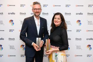 Man and woman holding awards in front of a sponsor’s board