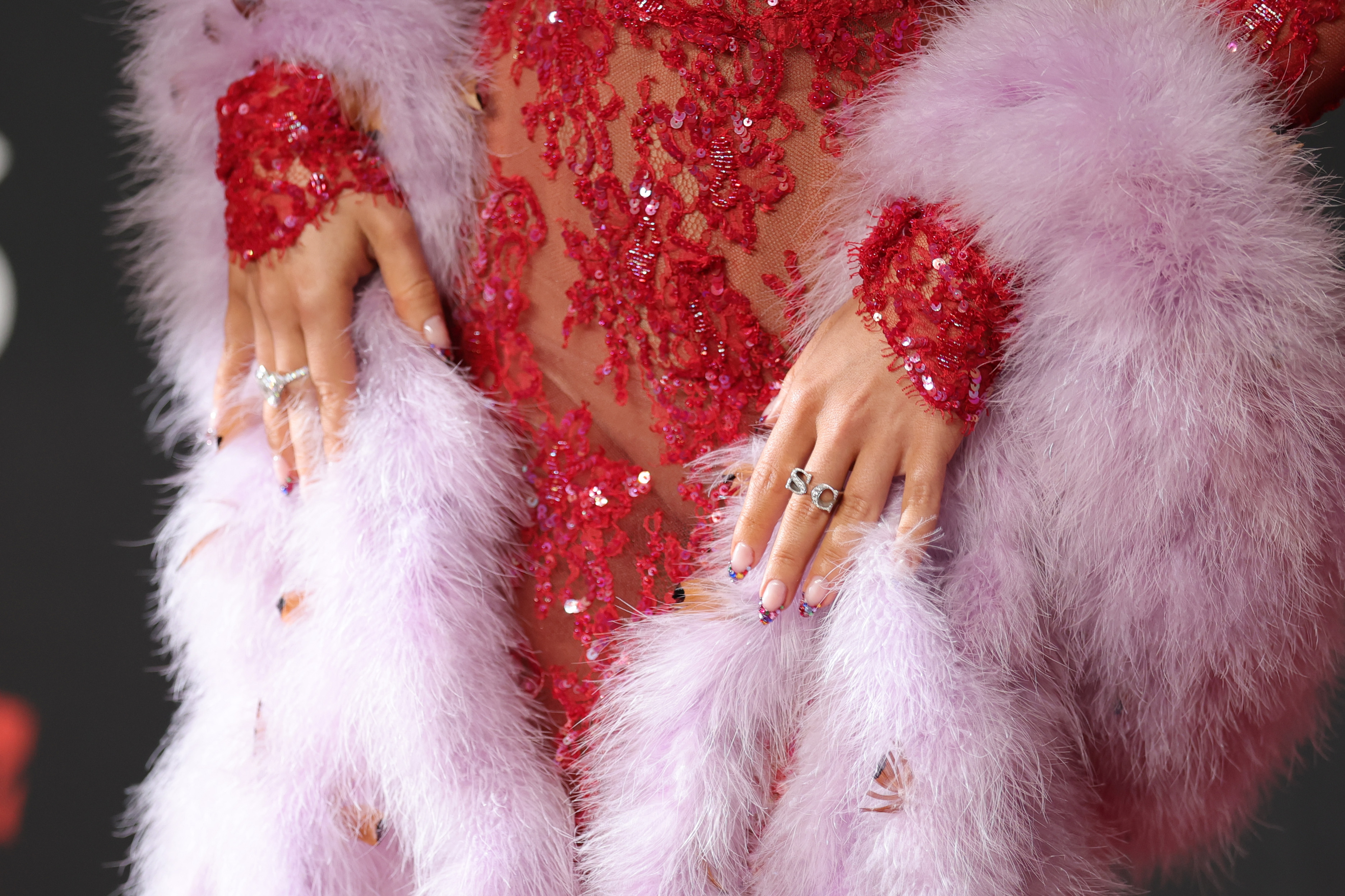 a woman&#039;s bedazzled french manicure pressed against a lacy red gown and pink fur shawl