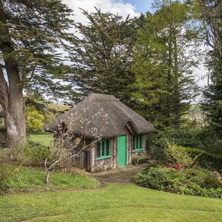 small cottage set in woods with a green door and thatched roof