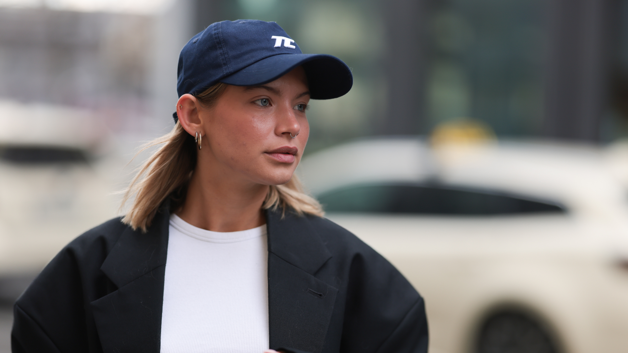 Sophia Geiss seen wearing Thesing navy blue sporty baseball cap, H&M cropped white cotton t-shirt, 032c oversized black relaxed wool coat with wide shoulders, on March 14, 2025 in Berlin, Germany.
