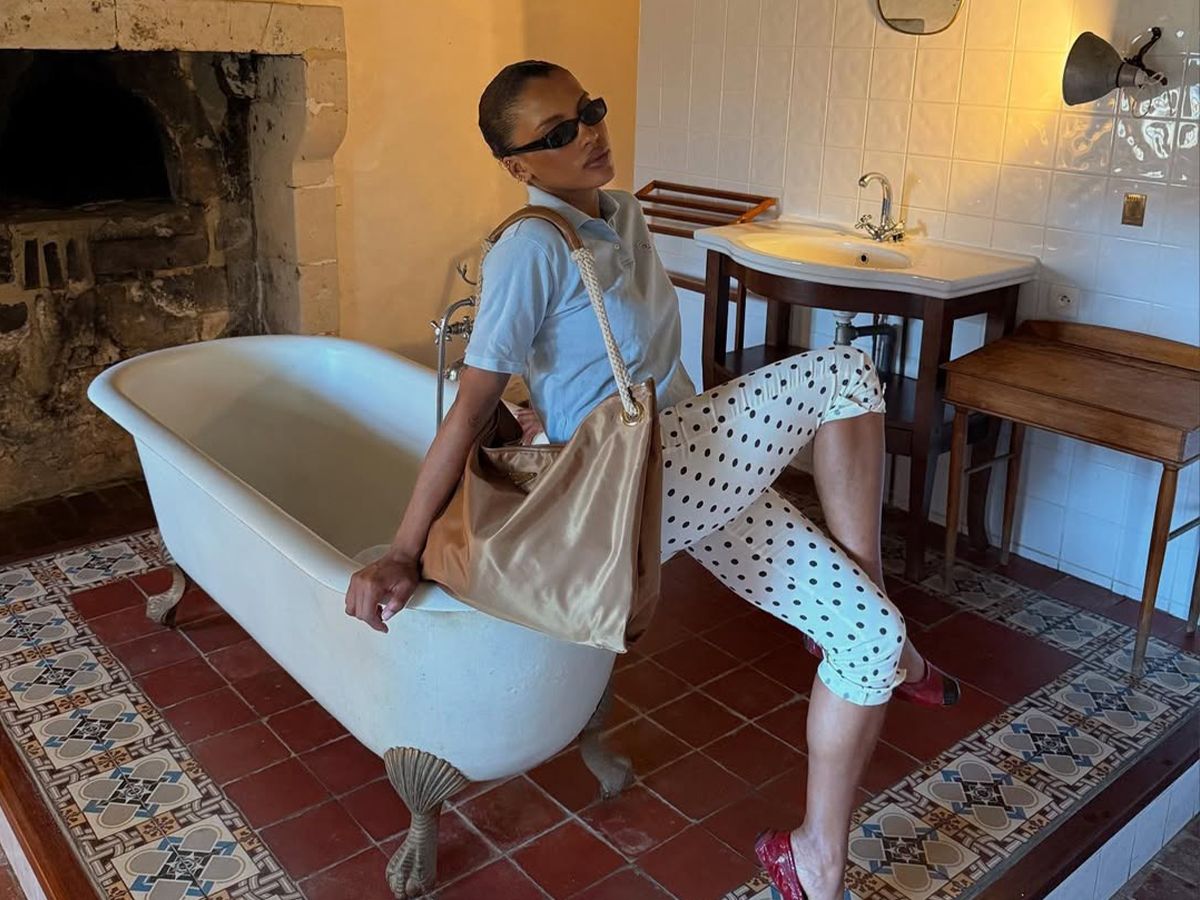 A woman sitting wearing polka dot capris, a gray polo, and a large gold tote.