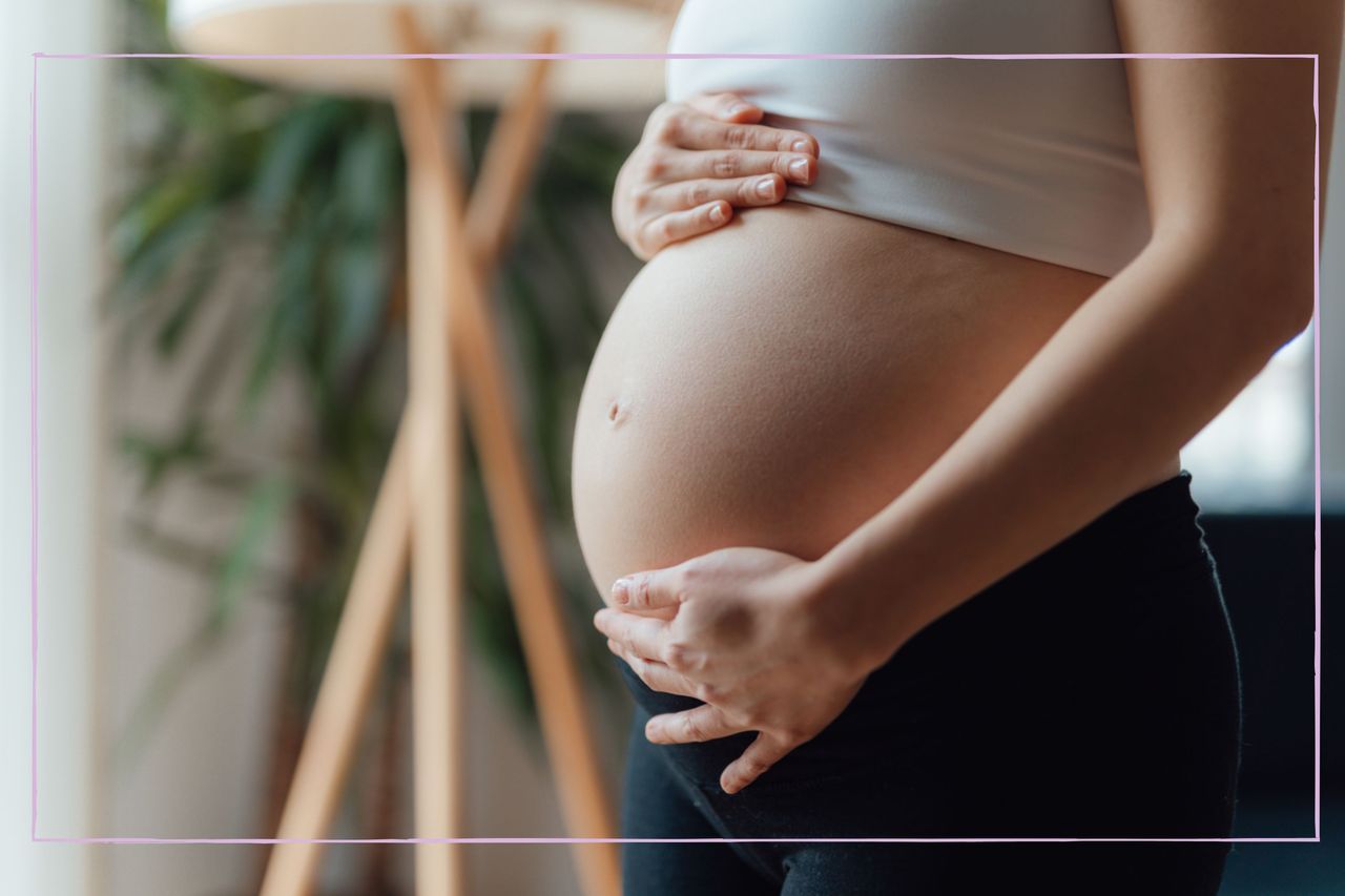 A close up of a pregnant woman&#039;s midsection as she hold her stomach