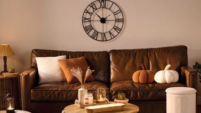 Brown sofa with pumpkin cushions. Round coffee table with diffuser and candles on top.