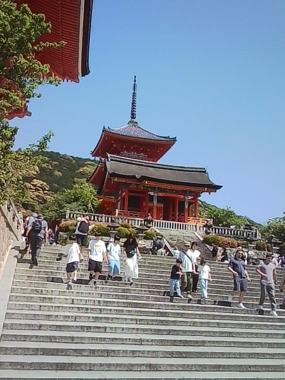 Visitors climbing wide stone steps toward a red pagoda-style temple in Japan.