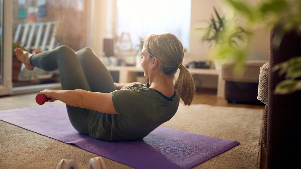 Woman performs the hundred exercise using dumbbells at home