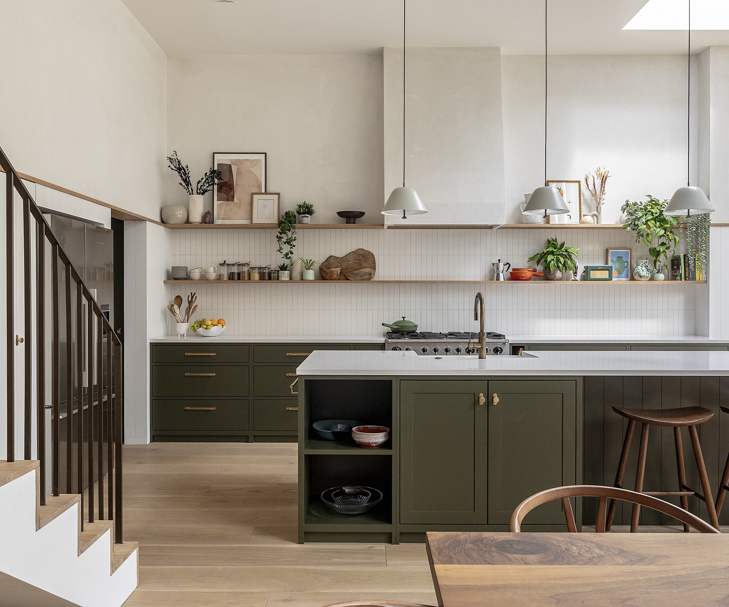kitchen with dark khaki cabinets and light surfaces and tiles. There are three pendant lights and a light oak floor
