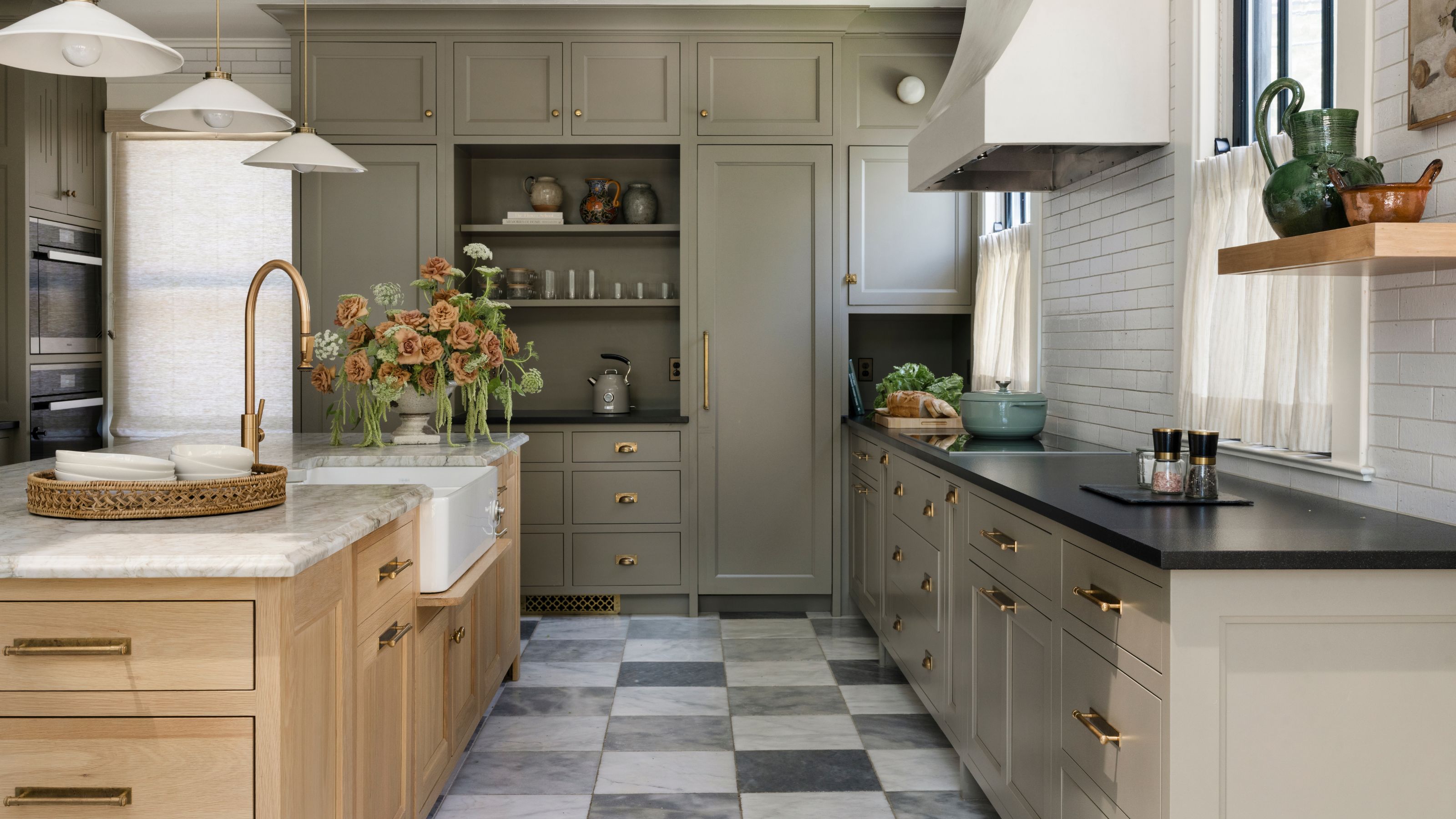 a grey green kitchen with checkerboard floors, oak island with marble counter and a trio of pendant lights