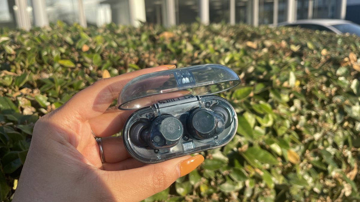 A pair of blue transparent Sony WF-C710N in their case being held in front of a hedge.