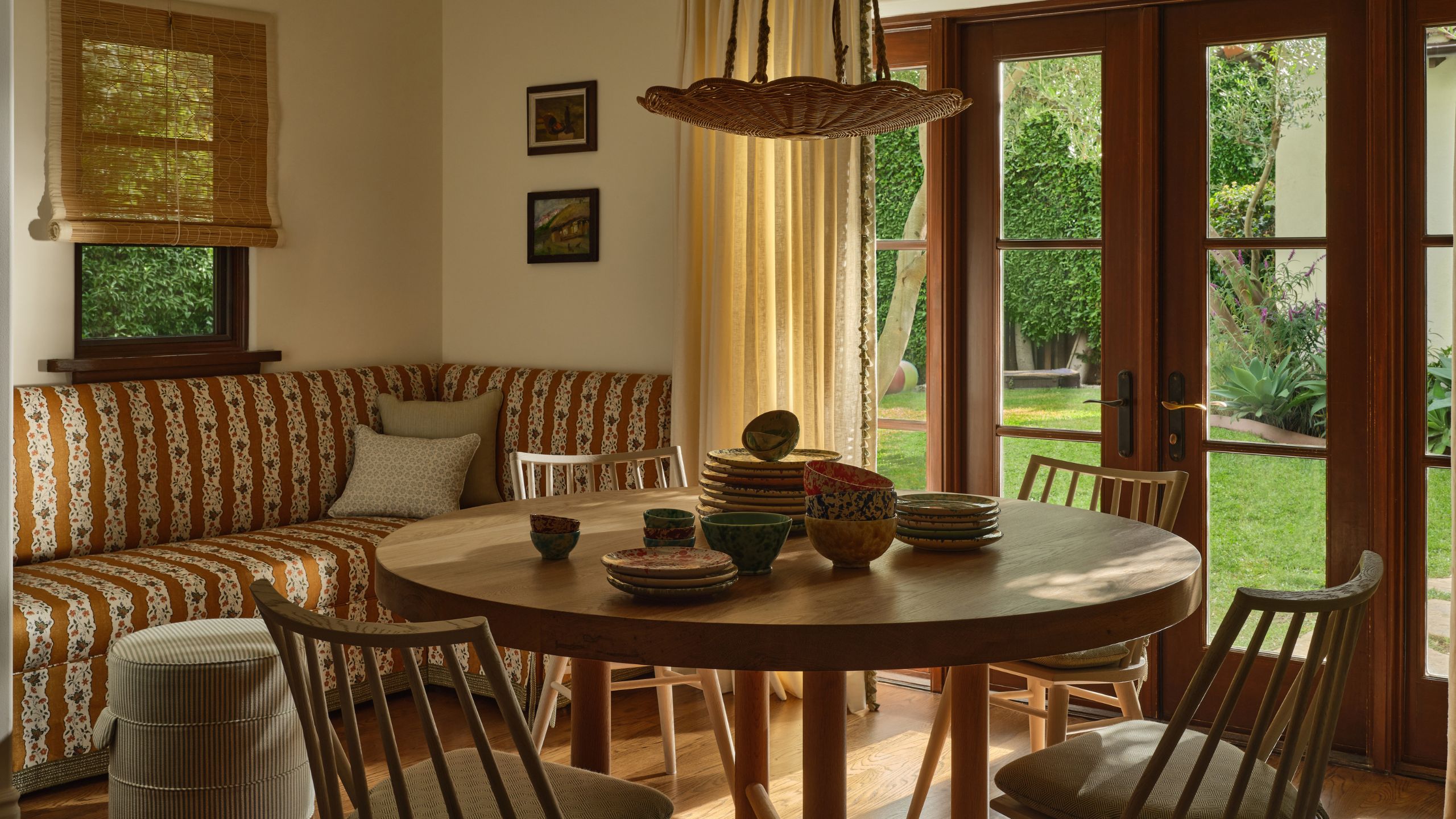 a cozy kitchen corner with orange floral striped banquette seat, wooden french doors and a round wooden table and chairs