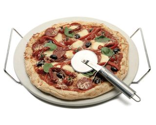 A round pizza stone set with rack and cutter and thin crust pepperoni pizza with olives, basil and mozzarella cheese