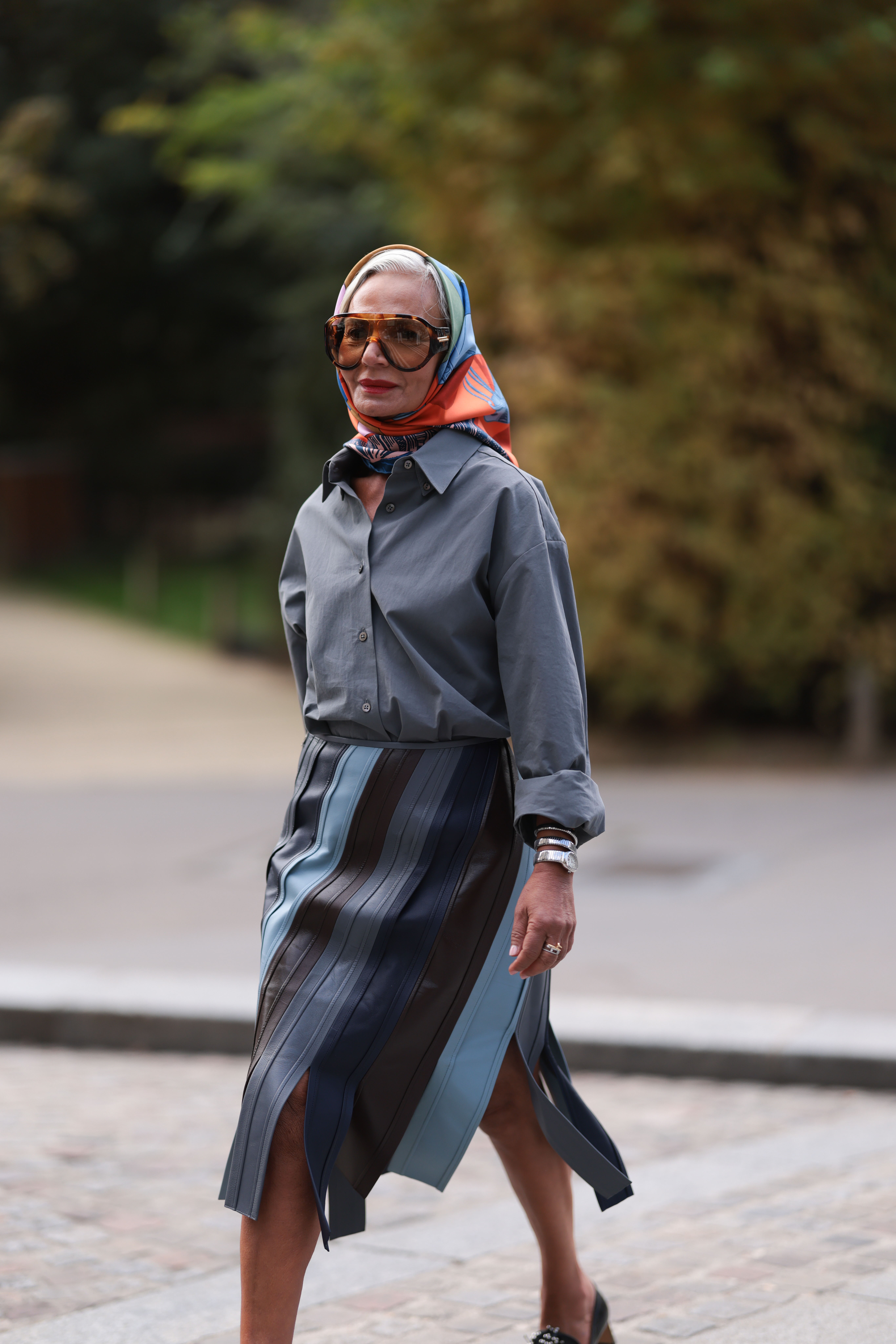 PARIS, FRANCE - SEPTEMBER 28: Grece Ghanem is seen wearing oversized shield frame sunglasses with havana frame, brown lenses, and wide temples from Bottega Veneta; a multicolored silk scarf around her head from Herm&amp;egrave;s; a grey oversized shirt, tucked into a midi leather skirt with wide fringes in blue shades from Bottega Veneta; a &amp;ldquo;Serpenti&amp;ldquo; watch from Bvlgari, with a silver helical bracelet and a snake-inspired shape; several rings in gold and silver; and black leather loafer pumps from Phoebe Philo before the Herm&amp;egrave;s Womenswear Spring/Summer 2025 Show as part of Paris Fashion Week on September 28, 2024 in Paris, France. (Photo by Jeremy Moeller/Getty Images)