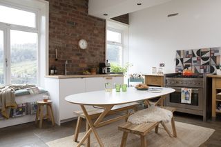 White kitchen-diner with exposed brick wall and oval wooden table and bench set