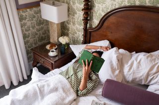 A woman reads a green hardcover book in bed at the Saratoga Arms boutique hotel in Saratoga Springs, New York