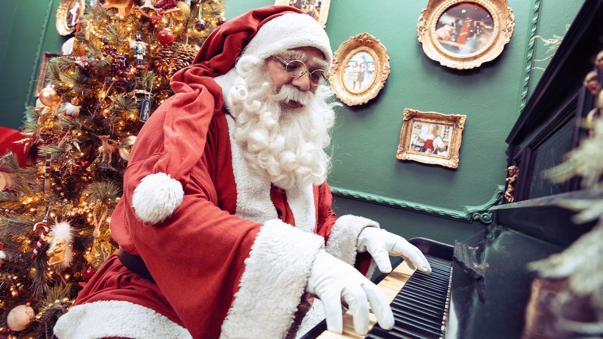 Santa Claus playing piano in front of a Christmas tree