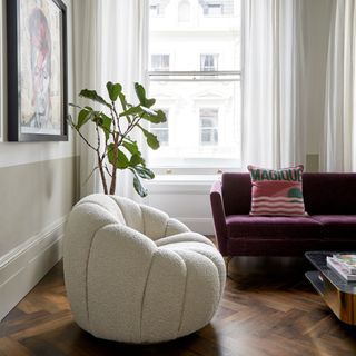 Living room with white boucle armchair, sofa, and large plant
