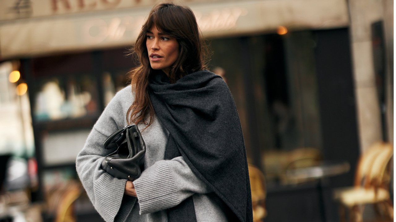 woman wearing grey sweater with dark grey cape carrying black handbag 