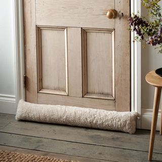 The White Company Curly Sheepskin Draught Excluder on wooden door with wooden floors
