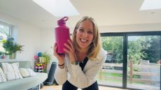 Woman smiling at camera holding large pink water bottle to the side of her face