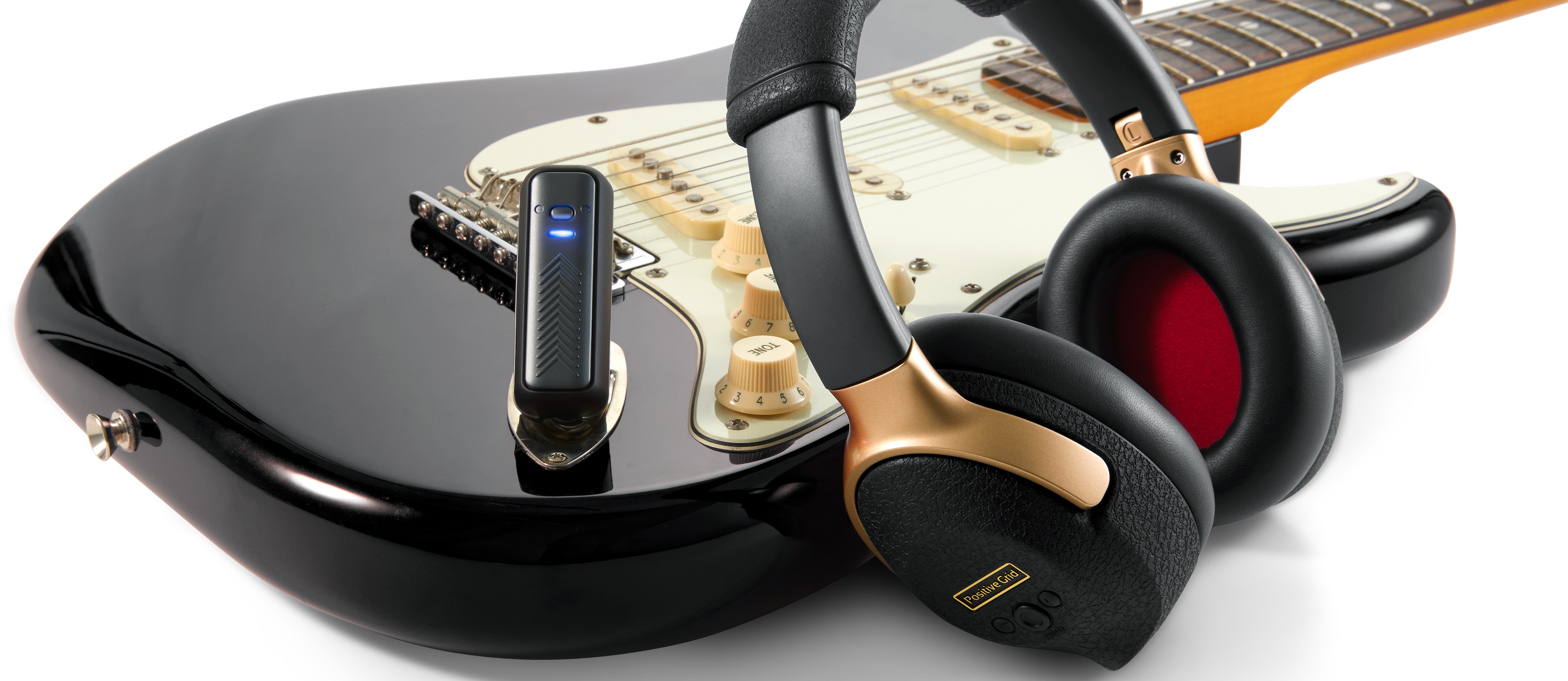 A photo showing the Positive Grid Spark NEO headphones and dongle with a black Stratocaster or Stratocaster-style guitar