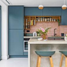 a contemporary dark blue kitchen with concrete kitchen island, bar stools and pendant lights with a pink graphic tiled splashback