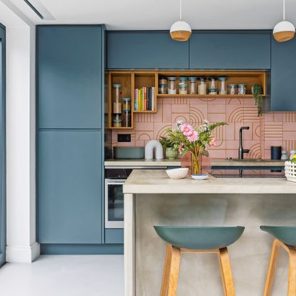 a contemporary dark blue kitchen with concrete kitchen island, bar stools and pendant lights with a pink graphic tiled splashback