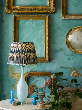 living room with painted wall mural in teal and turmeric, table lamp with pleated shade gold vintage frames