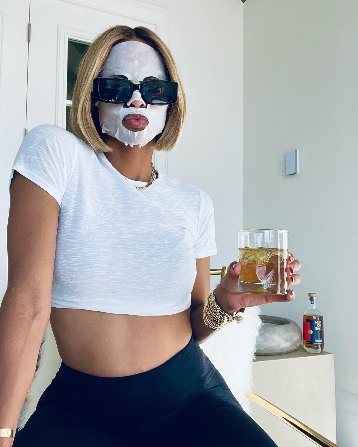 Ciara wearing a face mask with a glass in her hand and a linen blonde bob hairstyle