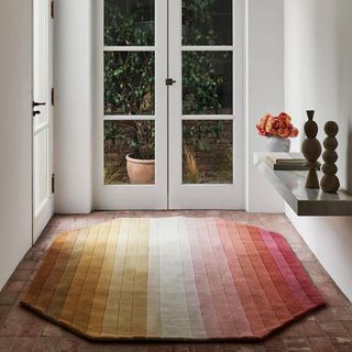 An ombre rug in pink, yellow, white sits on a wooden floor