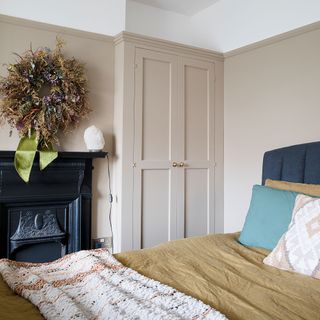 Neutral bedroom with built-in wardrobes, fireplace, blue upholstered bed, dried flower wreath