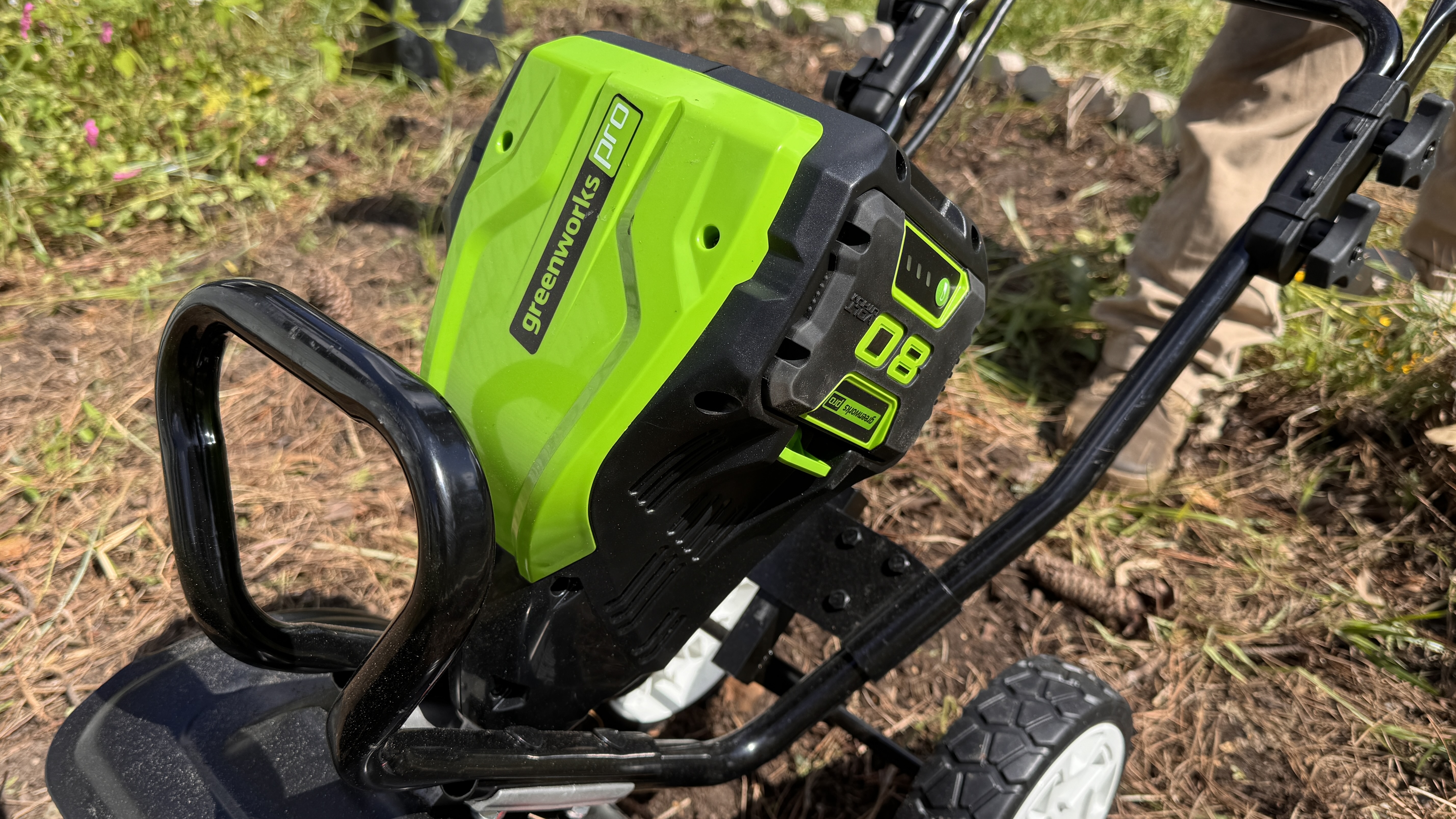 Closeup of GreenWorks tiller being pushed by man wearing brown pants