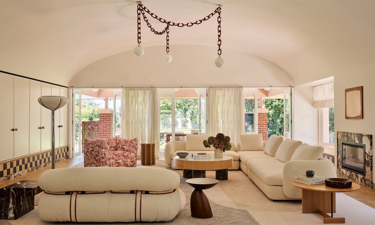 Living room with curved ceiling, curved cream sofas, wood side tables and chain chandelier
