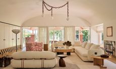 Living room with curved ceiling, curved cream sofas, wood side tables and chain chandelier