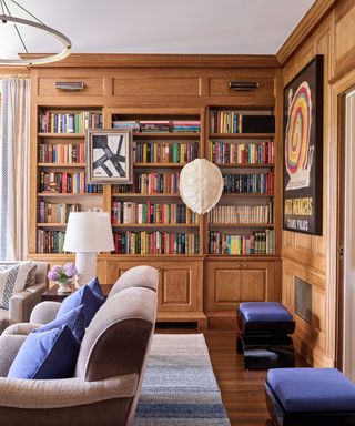living room with oak paneling and book shelves, neutral armchairs with blue cushions, blue stools and brass light fitting