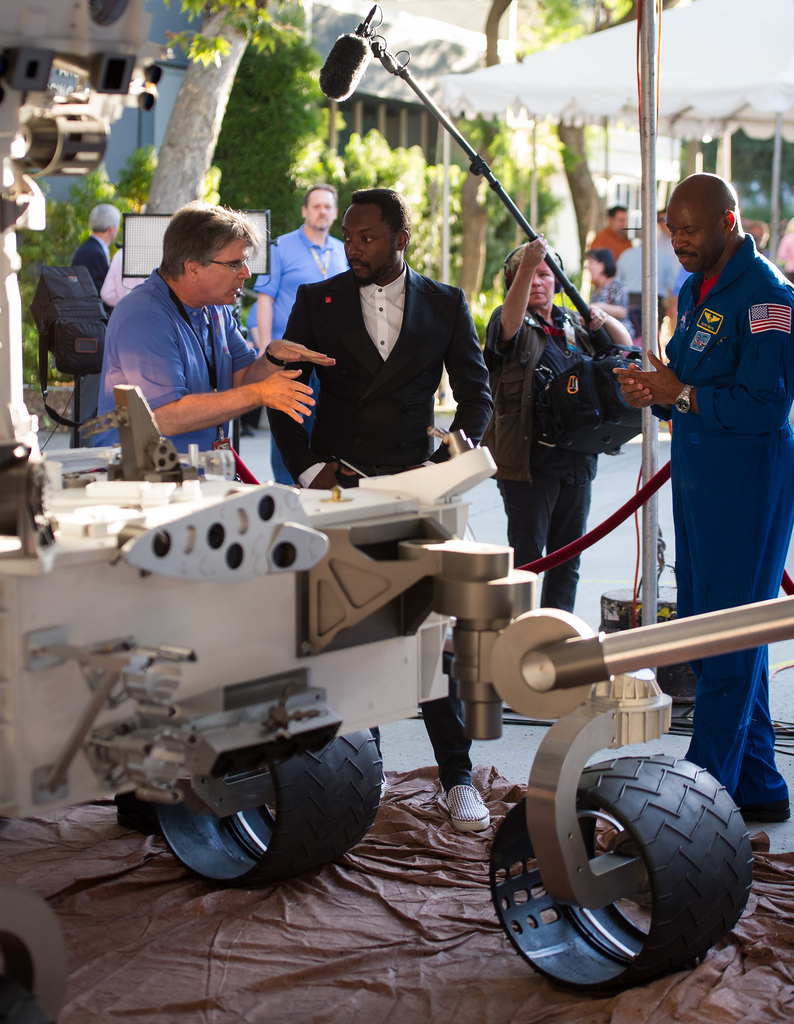 Musician Will.i.am, center, listens to NASA scientist Jim Garvin of the Goddard Space Flight Center talk next to a mock up of the Mars Science Laboratory rover Curiosity.